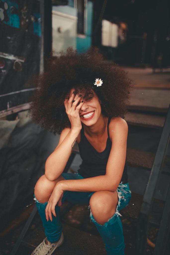 pexels-photo-1848565-1848565 Cheerful woman wearing ripped jeans and curly hair with flower, enjoying a sunny day outdoors.